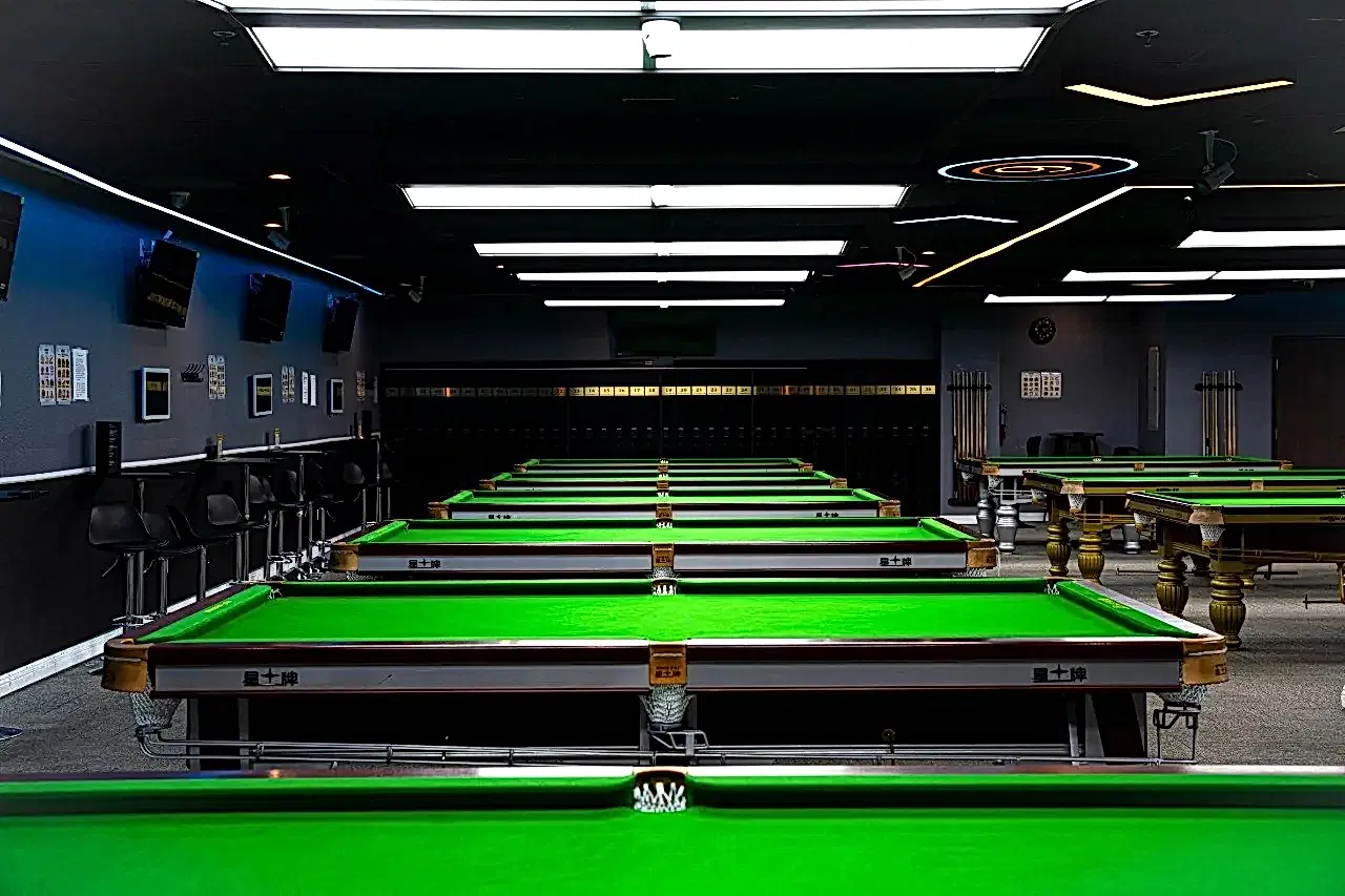 Rows of professional billiard tables and focused lighting inside iCUE Billiard Club